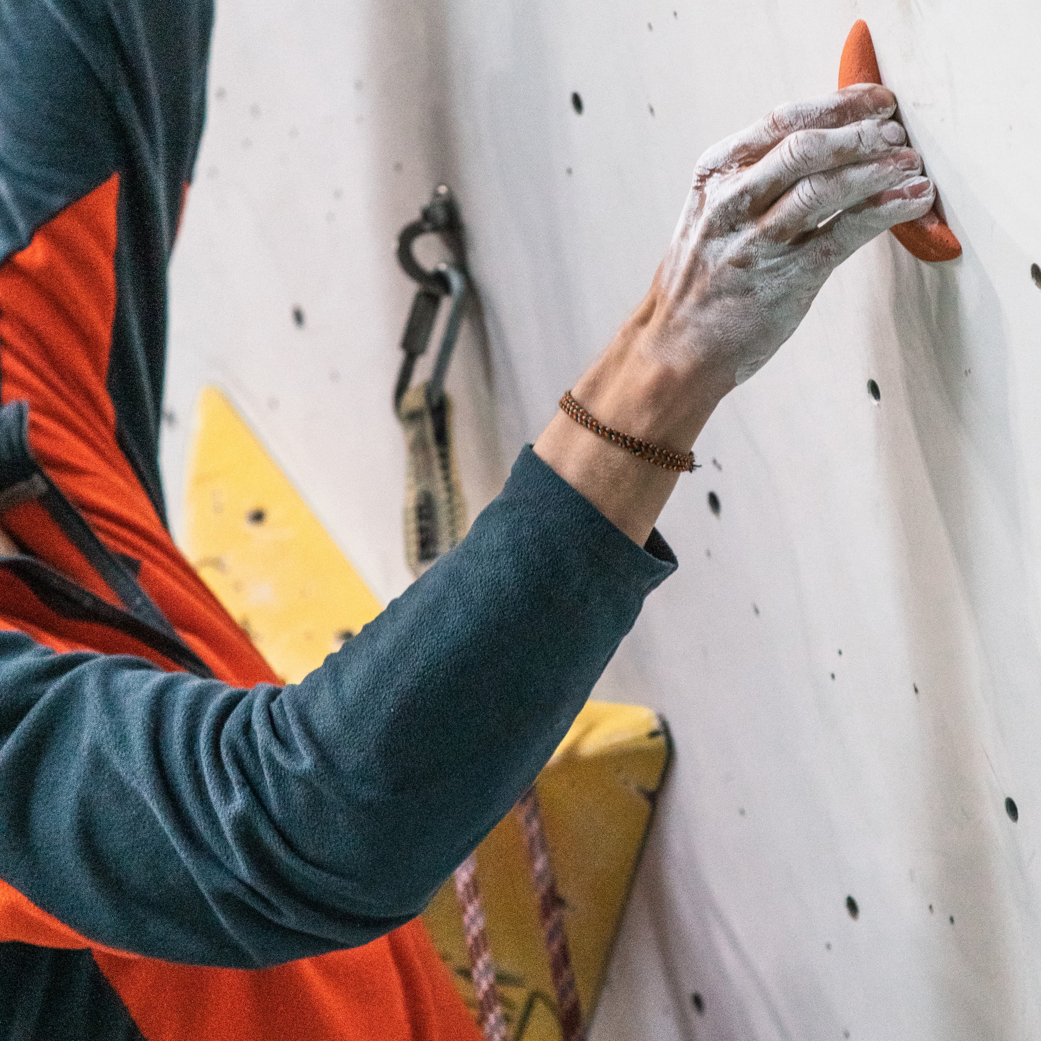 Chalked climber hand gripping a small hold on an indoor wall — finger strength and load management in climbing.